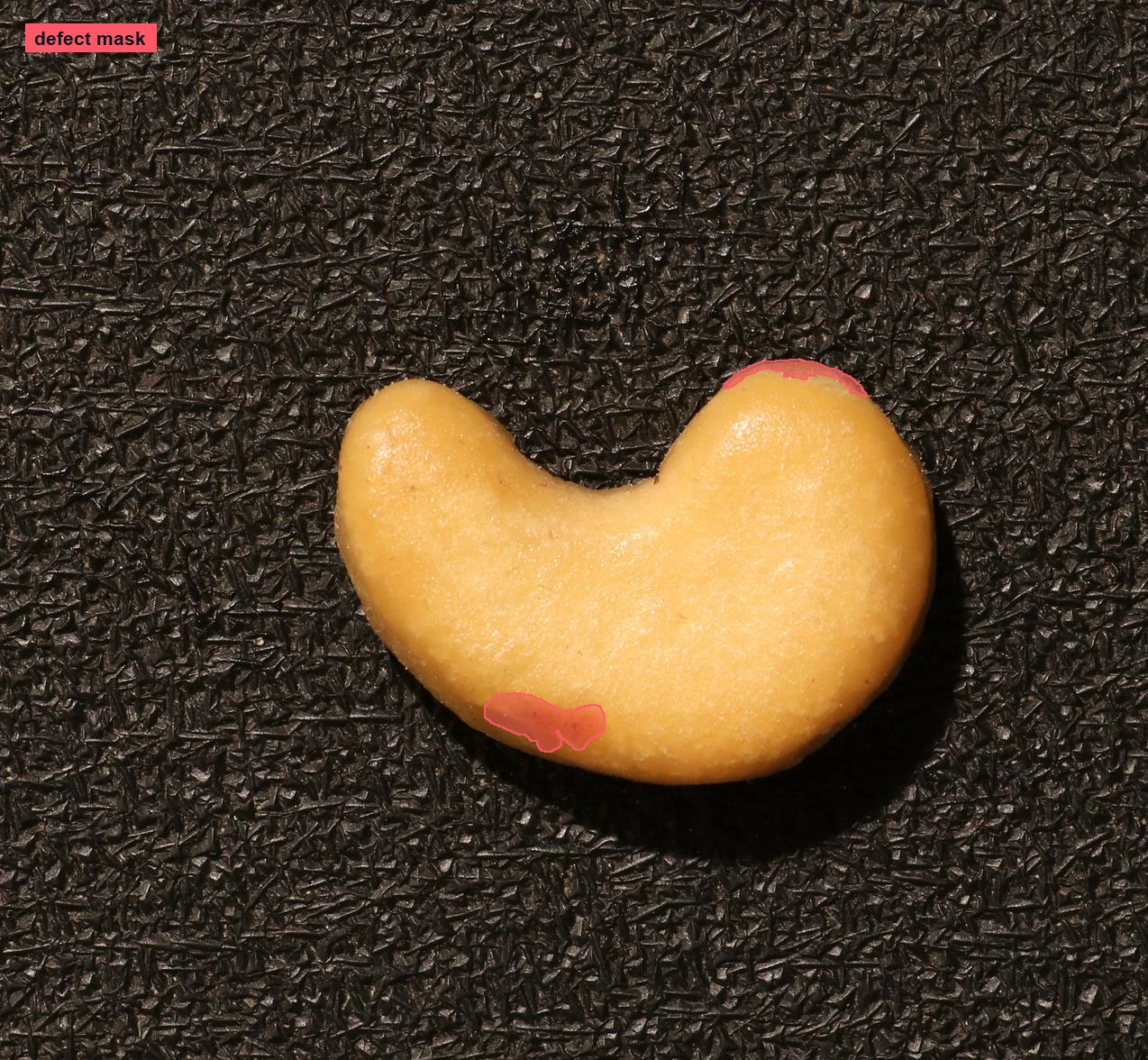Cashewnuss auf dunklem Untergrund mit rot markierten Fehlerbereichen an ihrer Kontur.